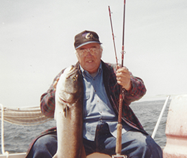 Bob, Steve's grandfather, in younger years, sitting on a boat holding up 2 rods and a fish.