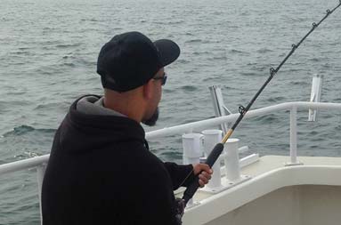 Another one of the guys sitting down on the boat reeling in a fish.
