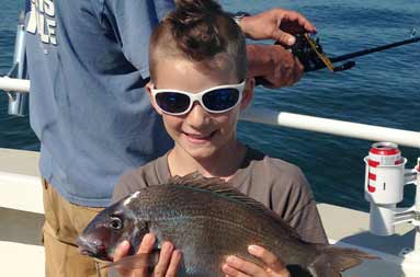 One of the kids holding up his scup and smiling with his sunglasses on