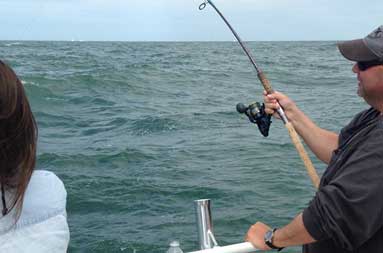 Capt TJ Montilli at the side of the boat with his line in the water reeling in a 40b bass