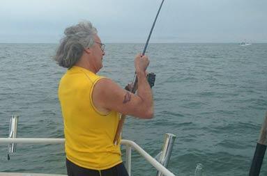Ken at the side of the boat with his line in the water reeling in a 45.5 bass