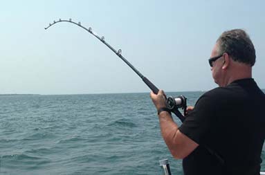 Marzio standing at the edge of the boat reeling in a fish