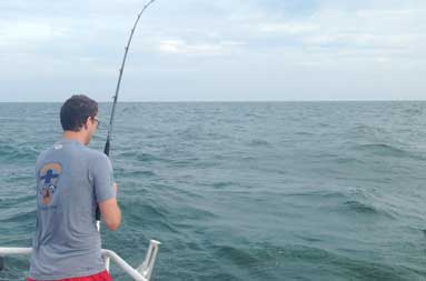 One of the guys standing at the edge of the boat reeling in a fish