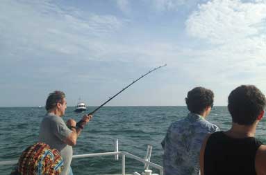 Another one of the guys standing at the edge of the boat reeling in a fish