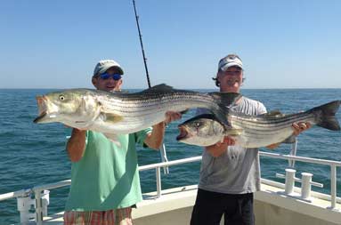 Two guys on the boat each holding up the large bass they caught