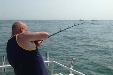 One of the guys at the edge of the boat with his line in the water