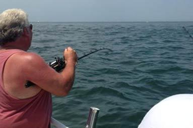 Kenny at the edge of the boat reeling in a fish