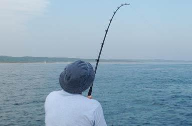 One of the guys reeling in a fish from the side of the boat