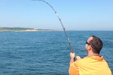 One of the guys reeling in a fish from the side of the boat