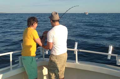 Reggie helping a younger kid reel in a fish