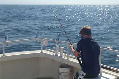 One of guys sitting at the edge of the boat with his line in the water
