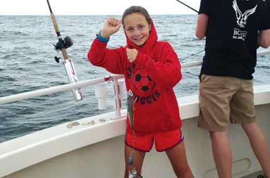 Adolescent girl in her red sweatshirt and shorts holding up her catch.