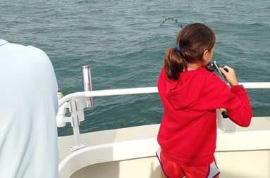 Back shot of same adolescent girl reeling in her catch