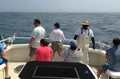 Shot of the back of the boat with Capt Gil standing with the guests already reeling them in.