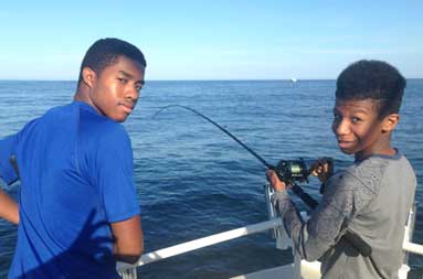 Two adolescent boys look back to the camera and smile as they fish