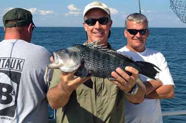One of the guys smiling looking at the camera holding his alb sea bass