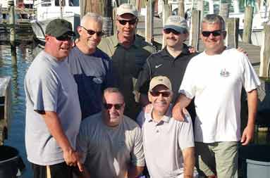 Group photo of the 7 guys back at the marina with some of their catch laid out in front of them