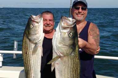 Two of guys smiling into the camera as they hold up their striped bass