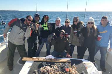 Group shot of everyone on the boat bundled up in fall/winter clothing on an sunny day with their fish filleted on the board in front of them