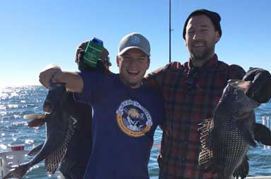 Two guys from the group smiling as they hold us the sea bass they caught.
