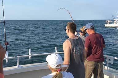 =View of the back of a young woman fighting to reel in a fish with other people watching.