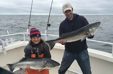 A man and young boy smile proudly as they each hold up their striped bass.