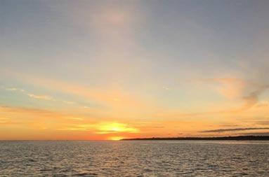 A sunset, with the vast ocean ahead and the sky with clouds in a yellowish-orange blue. 