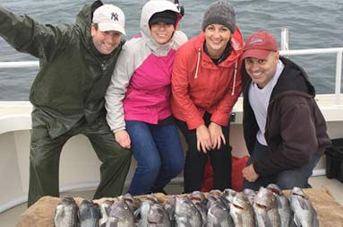 Group photo of two women and two men standing behind a spread of sea bass and smiling for the camera.