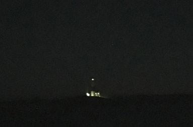 View from the boat in pitch blackness on the water before sunrise, the lights of the Montauk Lighthouse visible off in the distance.