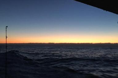 View from the boat looking out over the dark ocean, and the horizon as the sun just begins to rise in yellow and orange colors.
