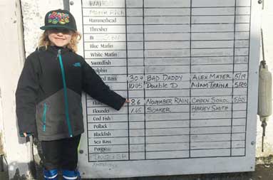 A young boy proudly weighing his fish at the marina and he got his name on the leaderboard.