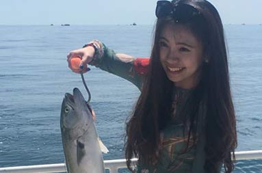 A woman aboard the boat holding the striped bass she caught giving a thumbs up.