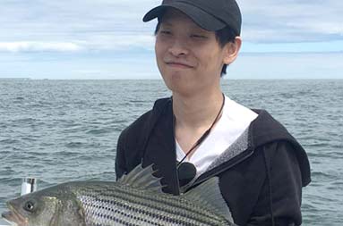 A young man holding up the striped bass he caught.
