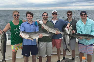 A group shot of six young men holding up their catch of striped bass.