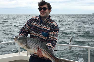 A man smiling big, holding up the fish he caught.