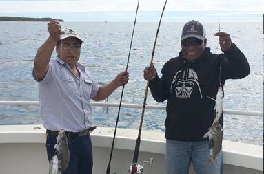 Two men holding up their reels and the fish they each caught.