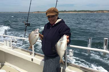 A woman smiling holding up the scup (porgy) she caught.