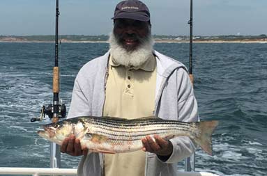 A man smiling holding up the scup (porgy) he caught.