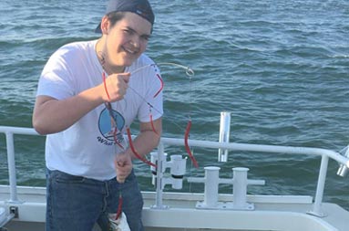 A young man shows off the two striped bass he caught on his line.