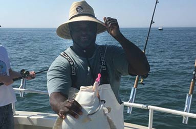 First mate, Gil, stands aboard the boat holding up an 8lb fluke .