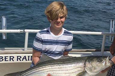 A young boy holds up the fish he caught and smiles for the camera.