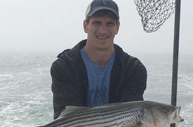 A man holding up the striped bass he caught.