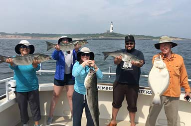 A group of 5 each hold up the striped bass and fluke they caught.