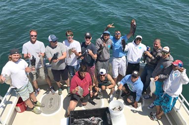 View from the top of the boat looking down at the deck at a large group of 14 men and their catch for the day.