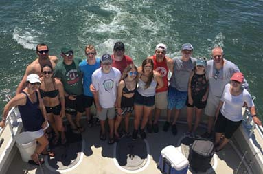 View from atop the boat looking down at the deck at the group of 14 men and women smiling for the camera.