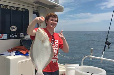 A young man wearing a red t-shirt proudly holds up the fluke he caught.