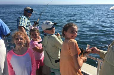 A group of kids fish as they look back to the camera and smile for a photo.
