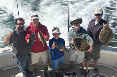 View from atop the boat looking down at the group on the deck holding the sea bass and fluke they caught.