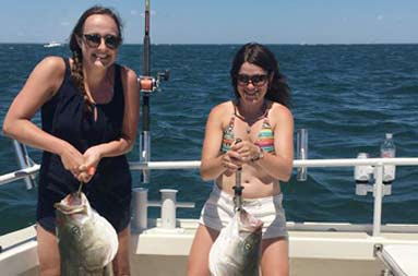Two women smiling as they each hold up the fish they caught.