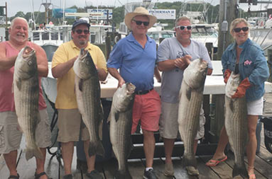 A group of 4 men and 1 woman back at the marina each holding up their catch.